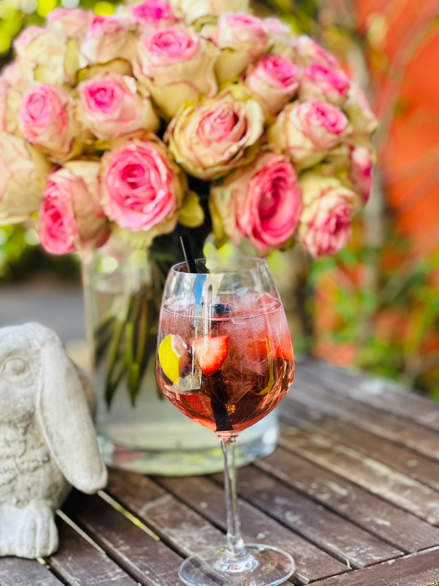 Sommerlicher Spritz mit Beeren neben rosa Rosen auf der Terrasse